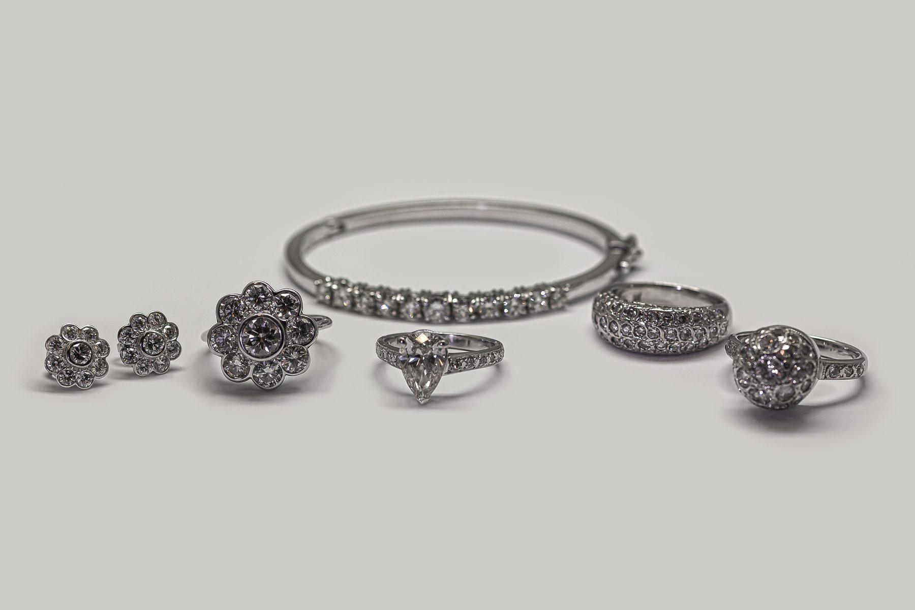 The Nicholson Goldsmiths bench, a bangle, halo cluster ring, princess solitaire, pave ring and diamond cluster earrings on a grey backdrop