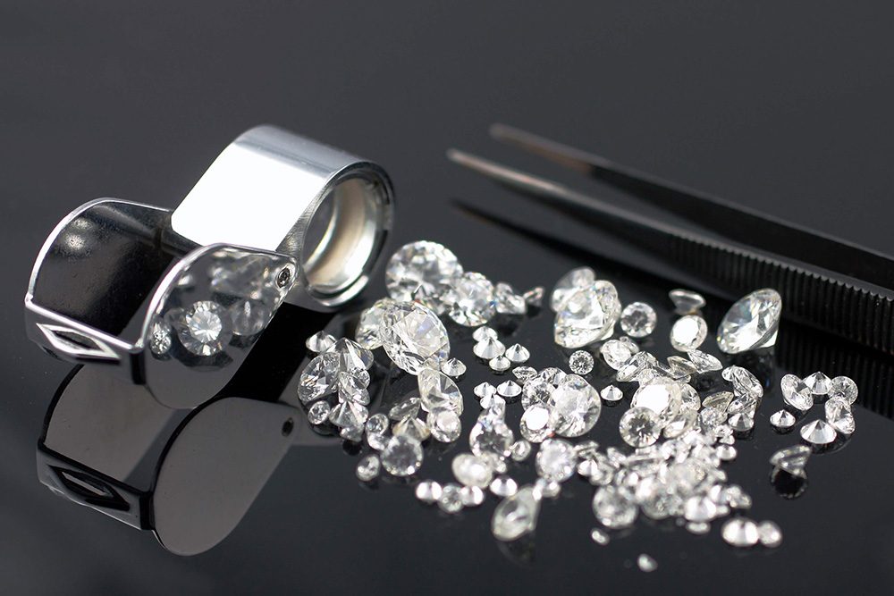 A jewellers loupe and tweezers next to loose diamonds on a black velvet pad at the Nicholson Goldsmiths bench, Beverley